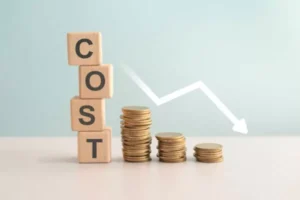 Wooden cubes with letters spelling "COST" arranged vertically next to coins.