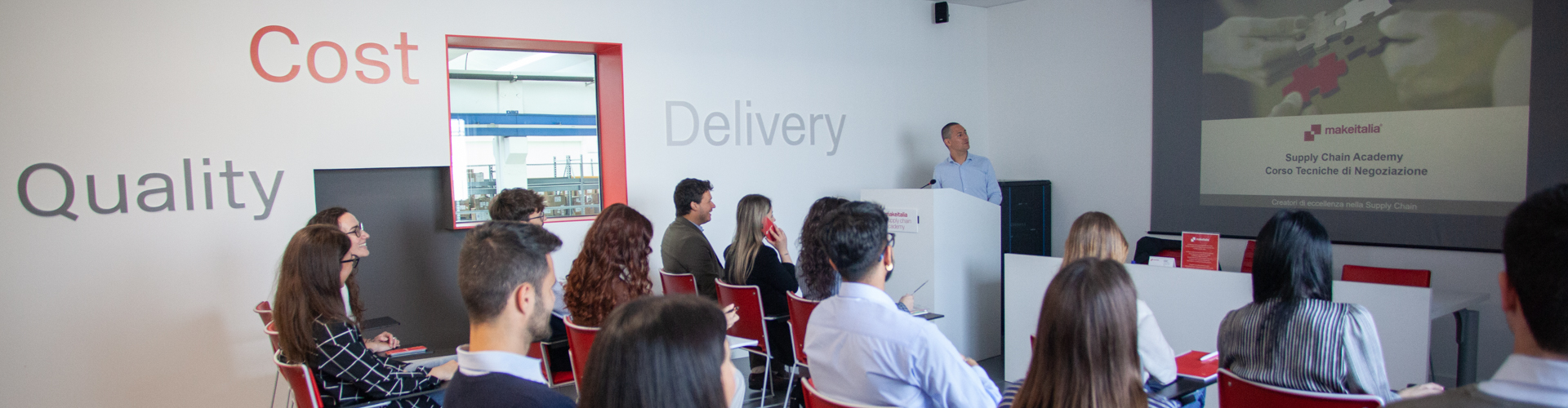 Persone sedute durante una presentazione aziendale o evento formativo con la scritta "Delivery" visibile sullo sfondo.