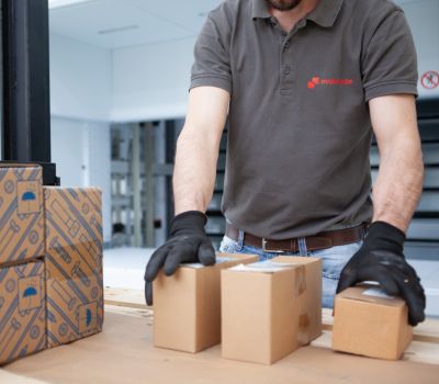 Un operatore con guanti protettivi che maneggia scatole di cartone, associato alla Supply Chain Factory di Makeitalia.